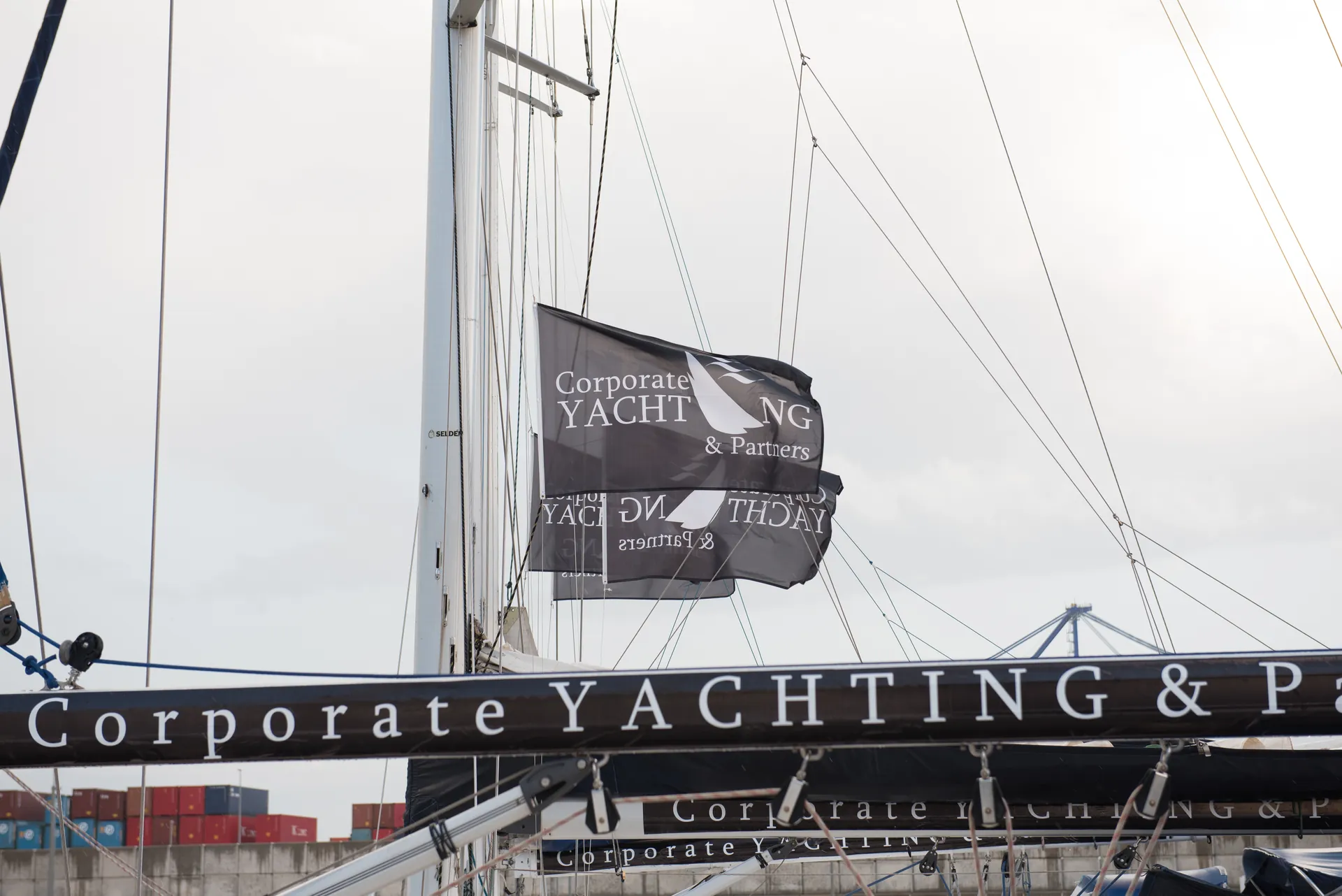 Gallardete de Corporate Yachting & Partners ondeando junto a la botavara del velero en el puerto.