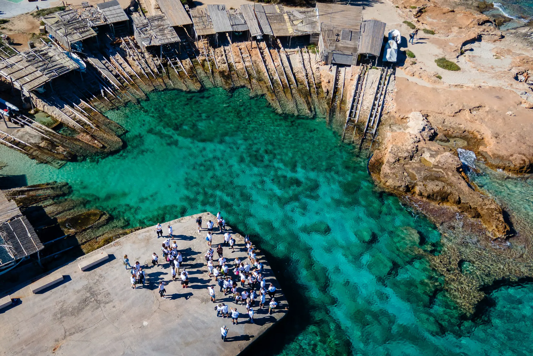 Vista aérea de los managers reunidos sobre un espigón junto a una cala de aguas turquesas.