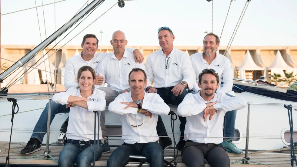 Retrato de equipo de siete personas con polo blanco a bordo del velero