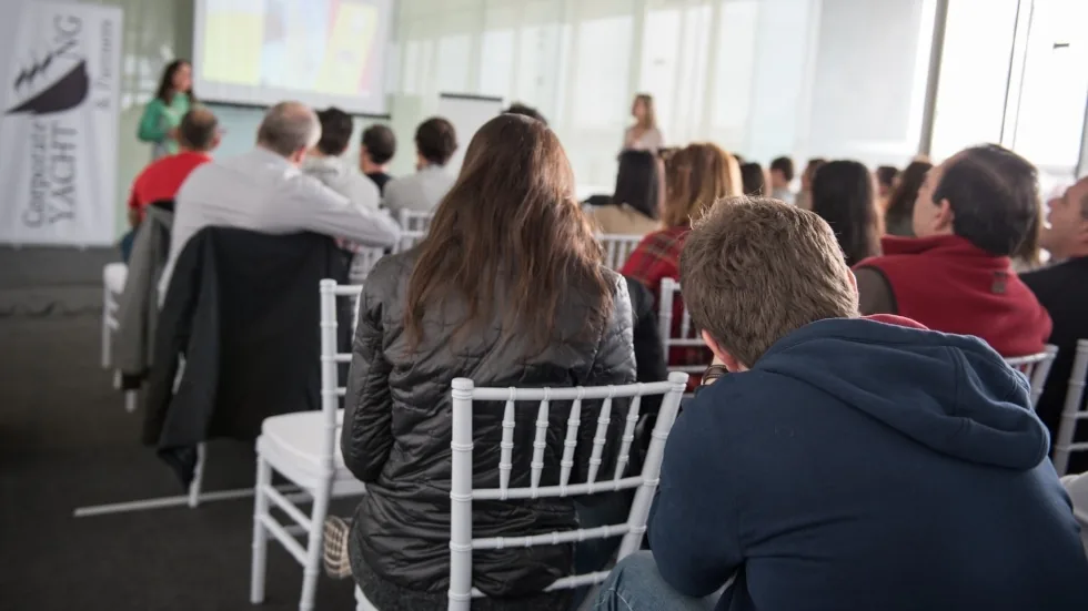 Público de espaldas siguiendo una presentación con proyector en una sala de formación