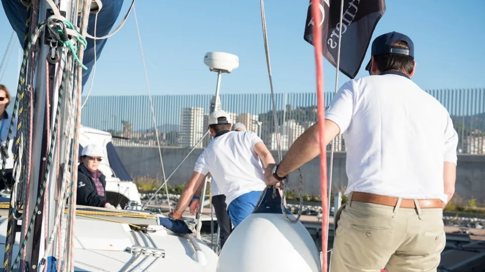 Tripulante sujetando un gallardete de Corporate Yachting en la cubierta del velero