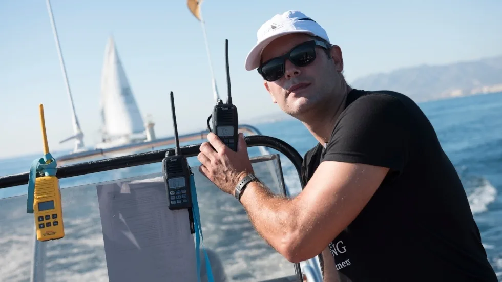 Tripulante sosteniendo dos emisoras VHF durante la coordinación de la regata