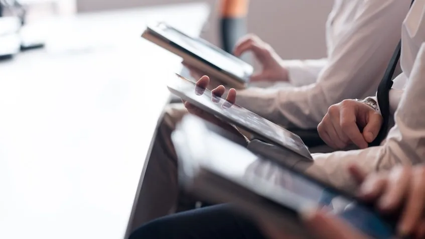 Personas sentadas en fila revisando documentos en tabletas, primer plano de las manos