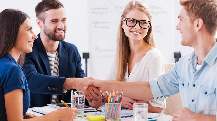 Cuatro profesionales dándose la mano alrededor de una mesa de reunión
