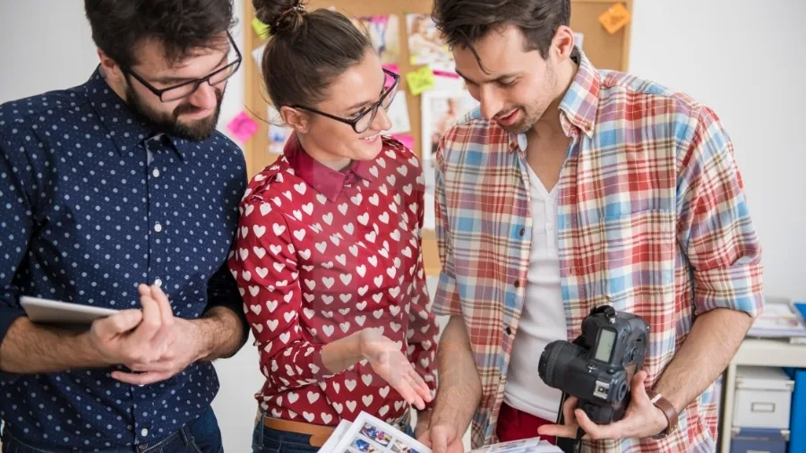 Tres compañeros de trabajo revisando fotografías con una cámara réflex en un despacho